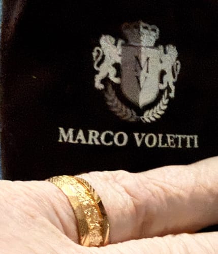 Close-up of a reviewer's hand wearing the textured gold Doreon ring, with the branded pouch shown behind it.