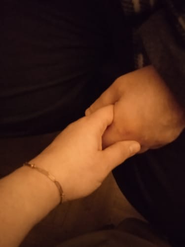 Reviewer's hand wearing a delicate gold-tone bracelet, holding another person's hand.