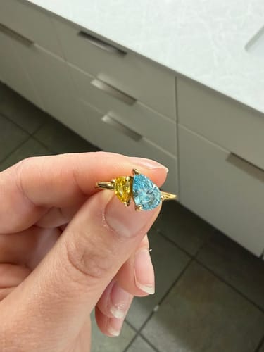 Customer holding the Leesha Birthstone Ring with yellow and light blue pear-cut stones on a gold band.