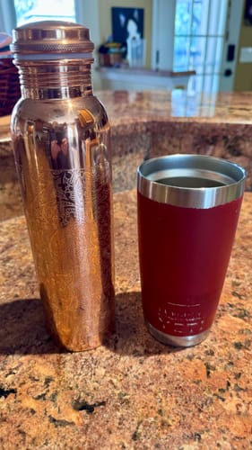 Customer's engraved copper water bottle shown for size next to a red tumbler on a counter.