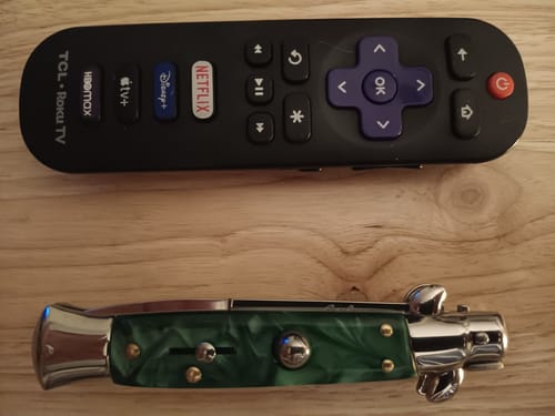Customer's folded Italian style switchblade with a green marbled handle, placed next to a TV remote for scale.