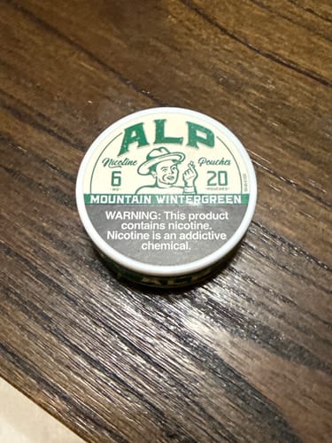 Customer's can of ALP Mountain Wintergreen Nicotine Pouches on a dark wooden surface.