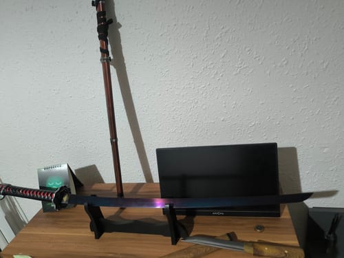Reviewer's Red Mortal Blade katana unsheathed on a black display stand, showing the blade's colorful finish.