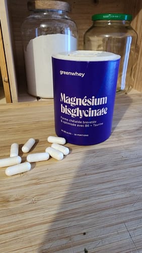 Client montrant le pot bleu de Magnésium Bisglycinate et des gélules blanches sur un comptoir en bois.