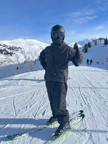 Reviewer wearing the black waterproof snow jacket on a sunny ski slope, giving a thumbs-up.