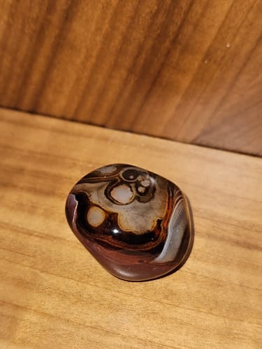 A customer's polished crystal with intricate brown, black, and cream patterns resting on a wooden surface.