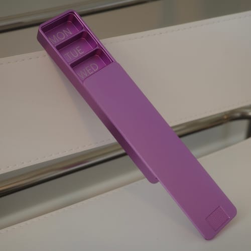 A reviewer's lavender Weekly Case shown partially open, revealing the empty compartments for Monday, Tuesday, and Wednesday.