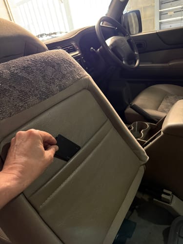 A customer's hand placing the SPOTMINDERS Tracking Card into the pocket on the back of a car seat.