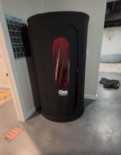Customer's black Sauna Pod 2.0 set up in the corner of a room, showing its compact, upright design.