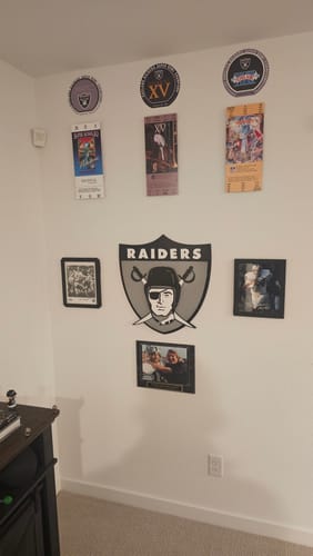 Customer's Las Vegas Raiders vintage shield art centered on a wall with other memorabilia in a fan cave.