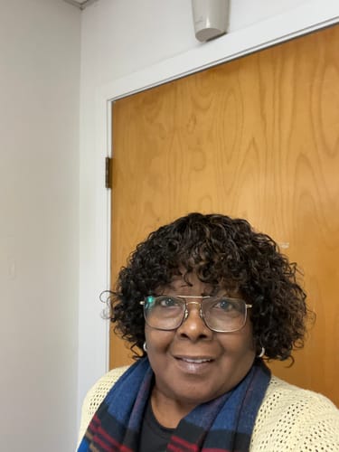 Reviewer smiling while wearing a dark, curly wig with bangs.