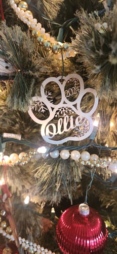 Reviewer's personalized pet ornament, shaped like a paw with 'Ollie' and '2024' cut out, hanging on a Christmas tree.