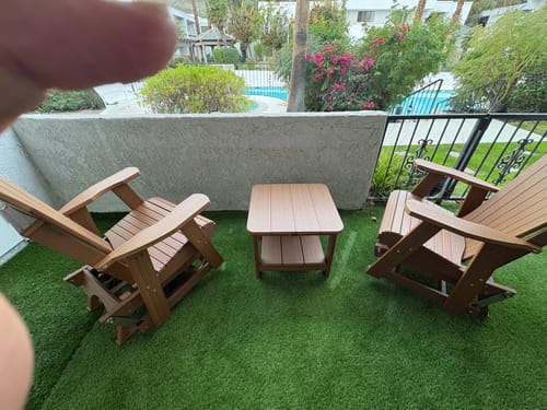 Partial view of customer's two light brown Adirondack gliders and end table on a patio with artificial turf.