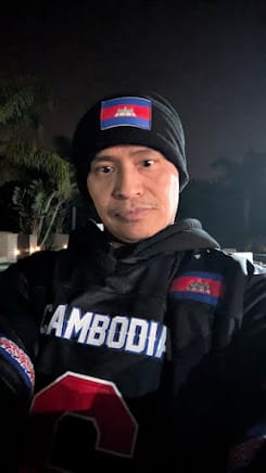 Customer wearing the black Cambodia Heritage Football Jersey and a matching beanie outdoors at night.