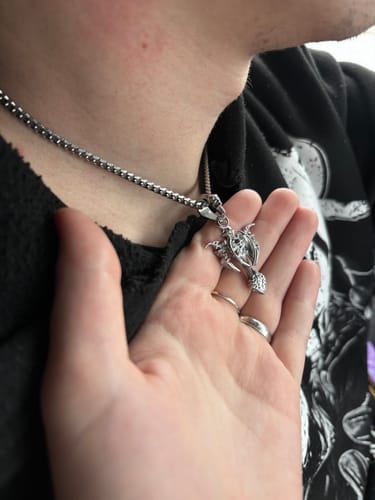 Reviewer holding up the silver TRIBAL CROSS PENDANT while a person wears it on a chain.