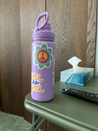 Customer's Retro Peace Flower Sticker on a purple water bottle sitting on a table.