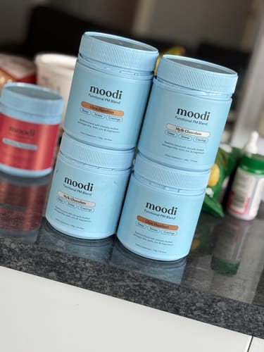 Customer's collection of four light blue jars of moodi Choc Hazelnut functional blend on a countertop.