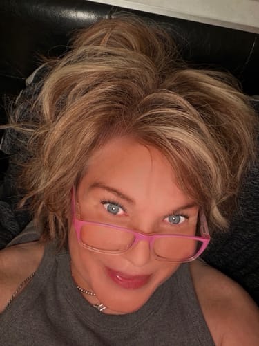 Close-up of a smiling reviewer with blonde hair wearing pink glasses.