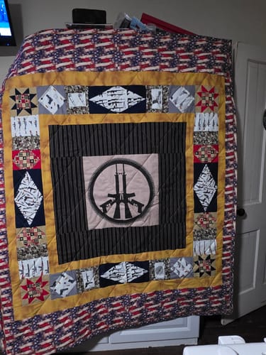 A reviewer's finished quilt made with the War & Peace Ammunition Silhouette Fabric Panel, showing a central design and flag border.