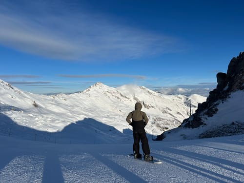 Customer wearing the waterproof Snow Jacket while standing on a snowboard overlooking a snowy mountain range.