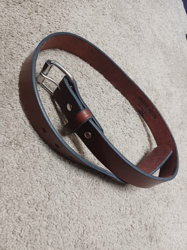 Customer's thick, reddish-brown Gunner belt with a silver buckle, coiled on a carpet.
