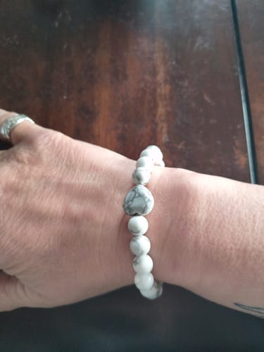 A reviewer's wrist wearing a white crystal bracelet with a marbled, heart-shaped bead.