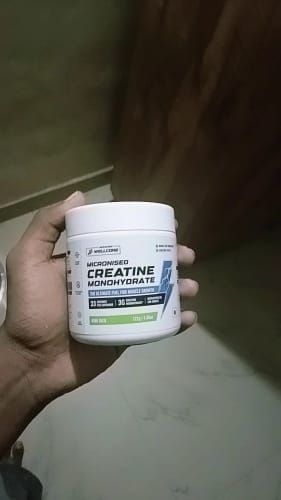 Reviewer holding a white tub of Wellcore's Micronised Creatine Monohydrate in the Kiwi Kick flavor.