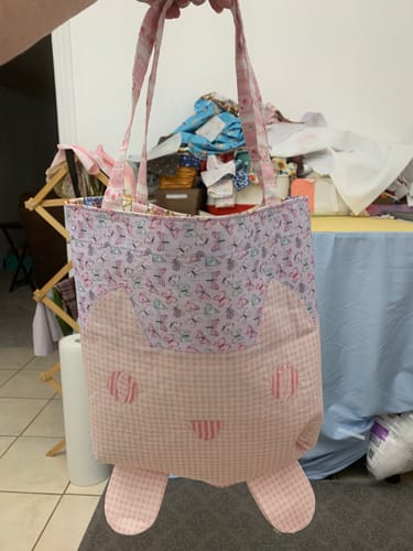 Customer holds a completed tote bag made from the Mrs Quilty Subscription Box, showing a cute cat face on a pink fabric.