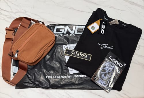 Customer's items from the Limited Overstock Drop: a black t-shirt, a brown bag, an air freshener, and a jet tag.