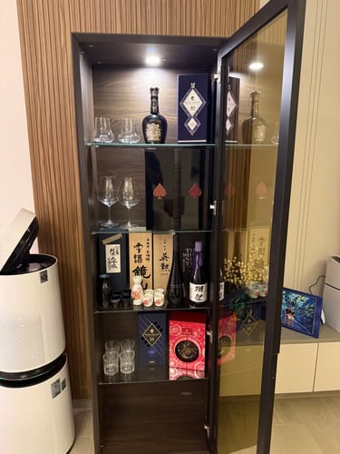 Customer's walnut Luis Wall Unit Glass Module with its door open, used as a lighted display cabinet for bottles and glasses.