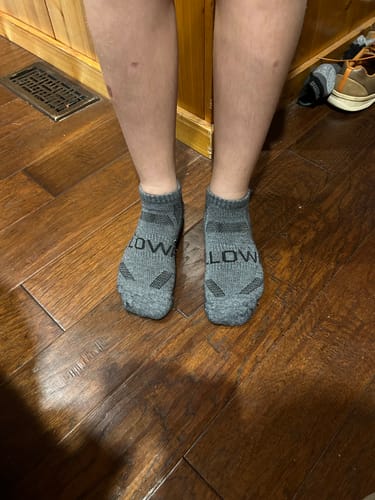 Customer wearing the grey, low-cut Men's Alpaca Socks while standing on a wood floor.