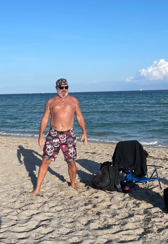 Customer on a beach wearing the comfortable White Red Sugar Skull Pattern Print swim trunks.