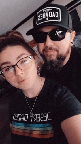 Reviewer wearing the black Mississippi Blackout Plate Hat in a close-up selfie with another person.