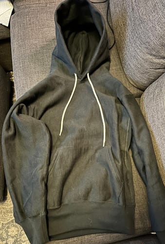 Customer's black Reverse Weave Hoodie with white drawstrings, laid flat on a couch to show its thick material.