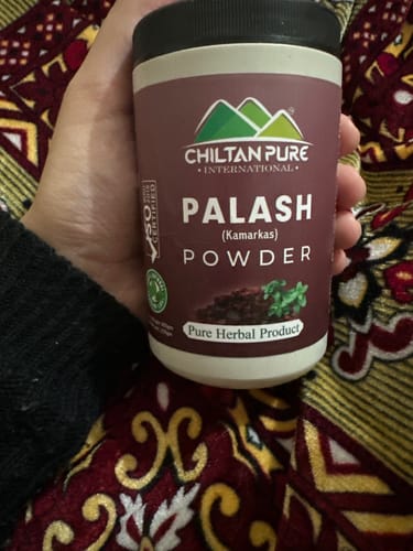 Reviewer holding a jar of Chiltan Pure Palash (Kamarkas) Powder against a patterned background.