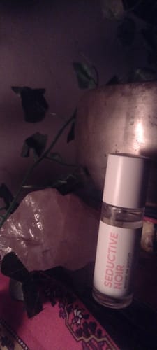 Customer's Seductive Noir fragrance bottle in a moody, dimly lit setting next to a large pink crystal.