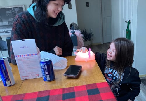 Customer's child smiles while touching the glowing Axolotl Squishy Night Light on a table.