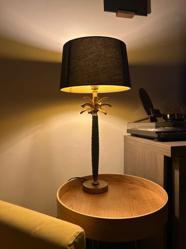 Klant toont de Areka tafellamp met zwarte kap, die aan staat op een houten bijzettafel.