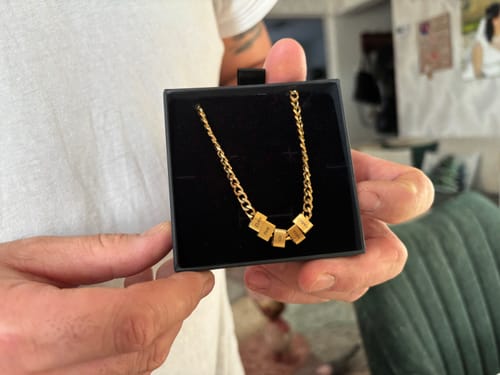 Customer holding an open black box showing the gold-colored Legacy Necklace with personalized beads.