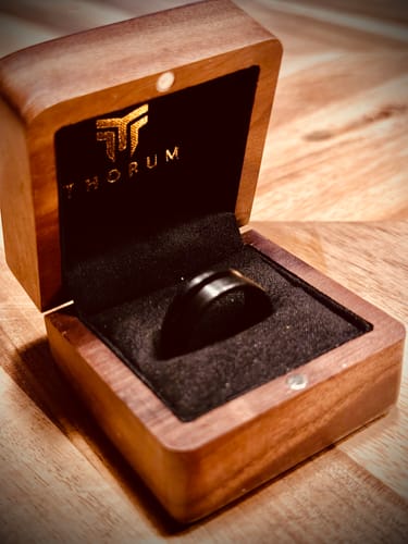 Customer's black Ancient Wood ring presented in an open, dark wooden Thorum brand box.