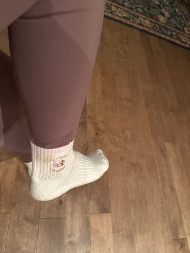 Close-up of a reviewer wearing the white ribbed 'All I Want Is Pilates' socks while standing on a wood floor.