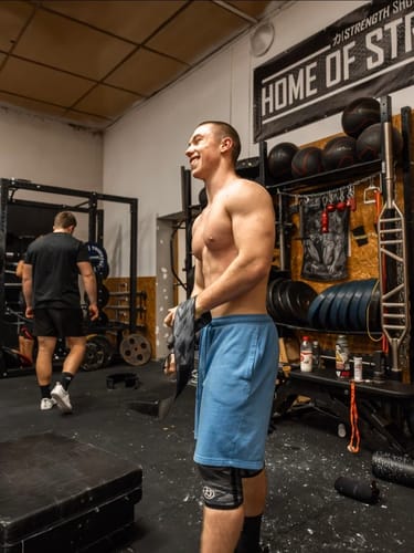 Reviewer smiling in a gym, holding the Dark Camo Medium Wrist Wraps.