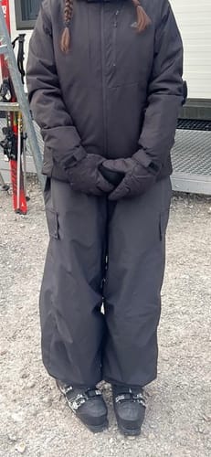 Reviewer standing outdoors in baggy black snow pants and ski boots.