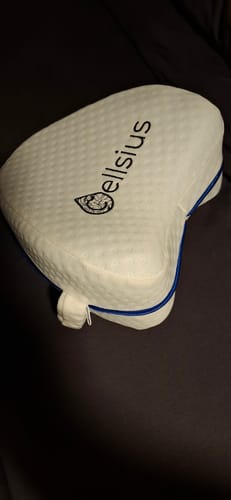 Un client montre son coussin orthopédique pour genoux Cellsius blanc, avec la sangle visible sur le côté.