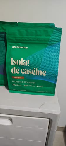 Sachet vert de l'Isolat de Caséine d'un client, saveur chocolat, posé sur une commode blanche.