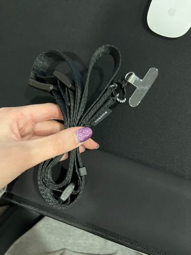 A reviewer's hand holding the coiled black Crossbody Phone Strap over a desk.