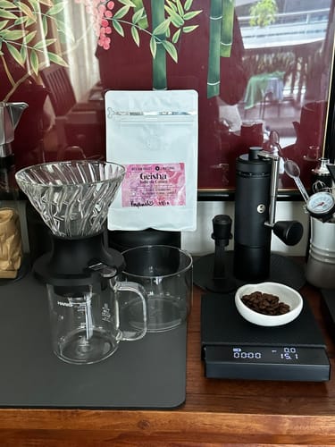 Reviewer's Geisha Colombia coffee pouch beside a grinder, scale with beans, and a complete pour-over coffee set.