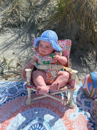 Customer's baby sits in the floral Paloma baby chair v2 on a beach.
