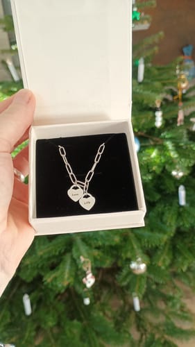 Ein Kunde hält eine offene Schmuckschachtel mit dem silberfarbenen Armband mit zwei personalisierten Herzanhängern darin.