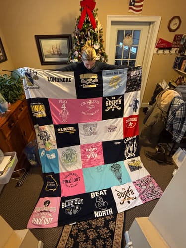 Reviewer holding up a large T-Shirt Quilt made from their high school field hockey and lacrosse shirts.